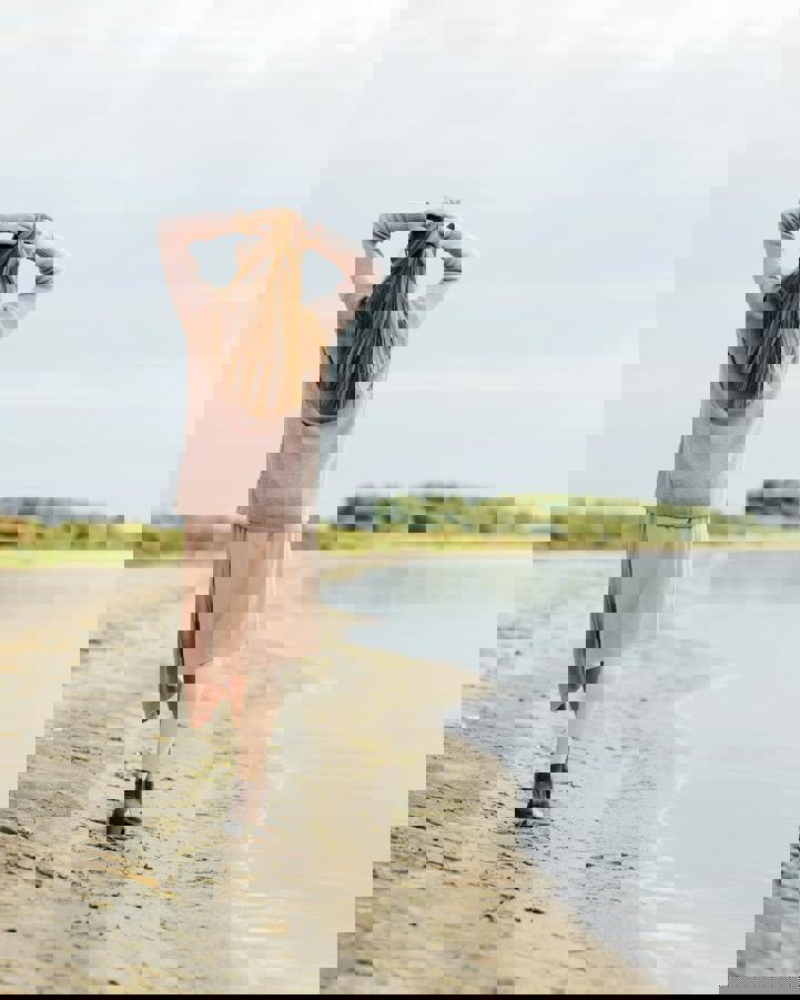 Blonde woman walking on lakeshore holding the back of her head